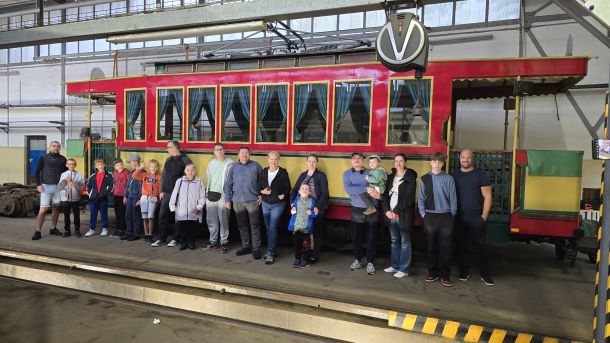 Zdjęcie odwiedzających zajezdnię tramwajową na tle tramwaju turystycznego