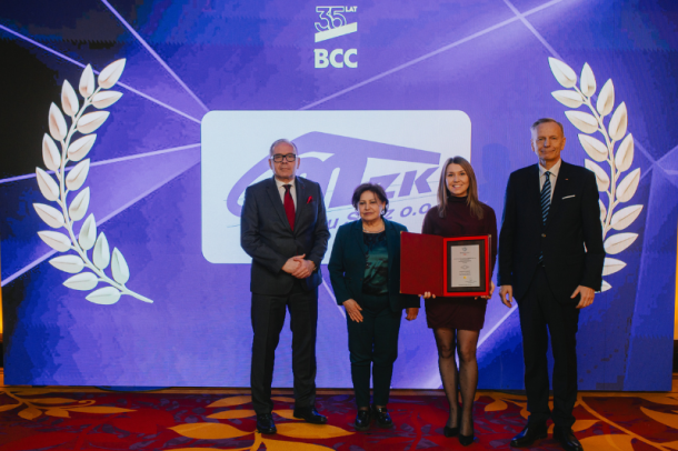 zdjęcie z rozdania nagród - cztery osoby na tle ścianki z logo MZK i BCC, jedna osoba trzyma nagrodę